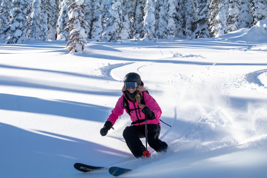 Advanced skier carving sharp powder turns on steep slope in Northern Rockies.