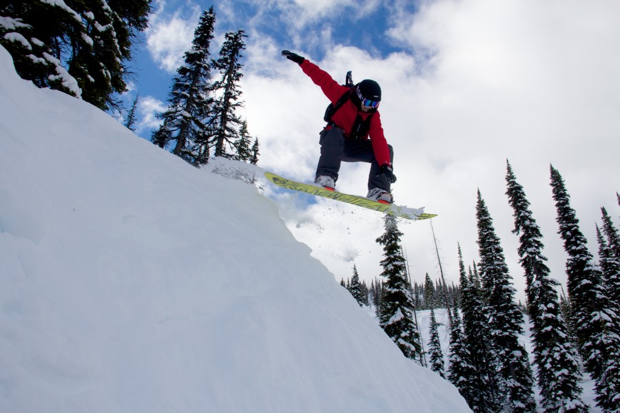 Snowboarder catching air off natural feature during Montana cat skiing adventure